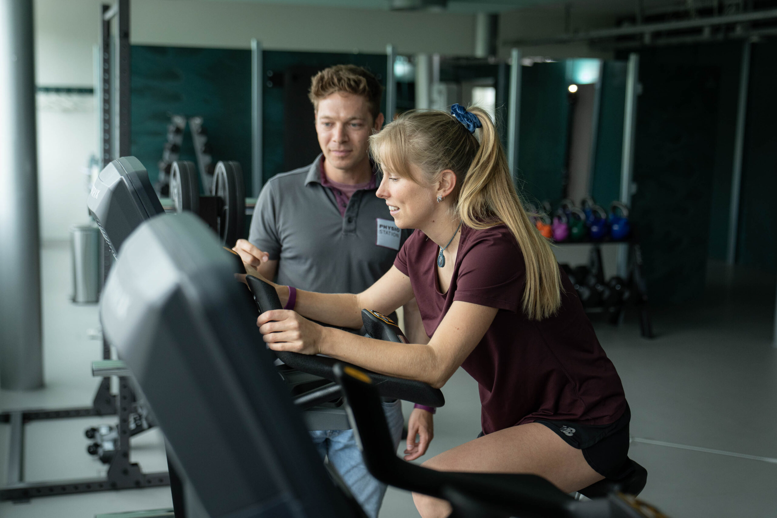 Physiotherapuet mit Patientin, die auf E-Gym Gerät trainiert